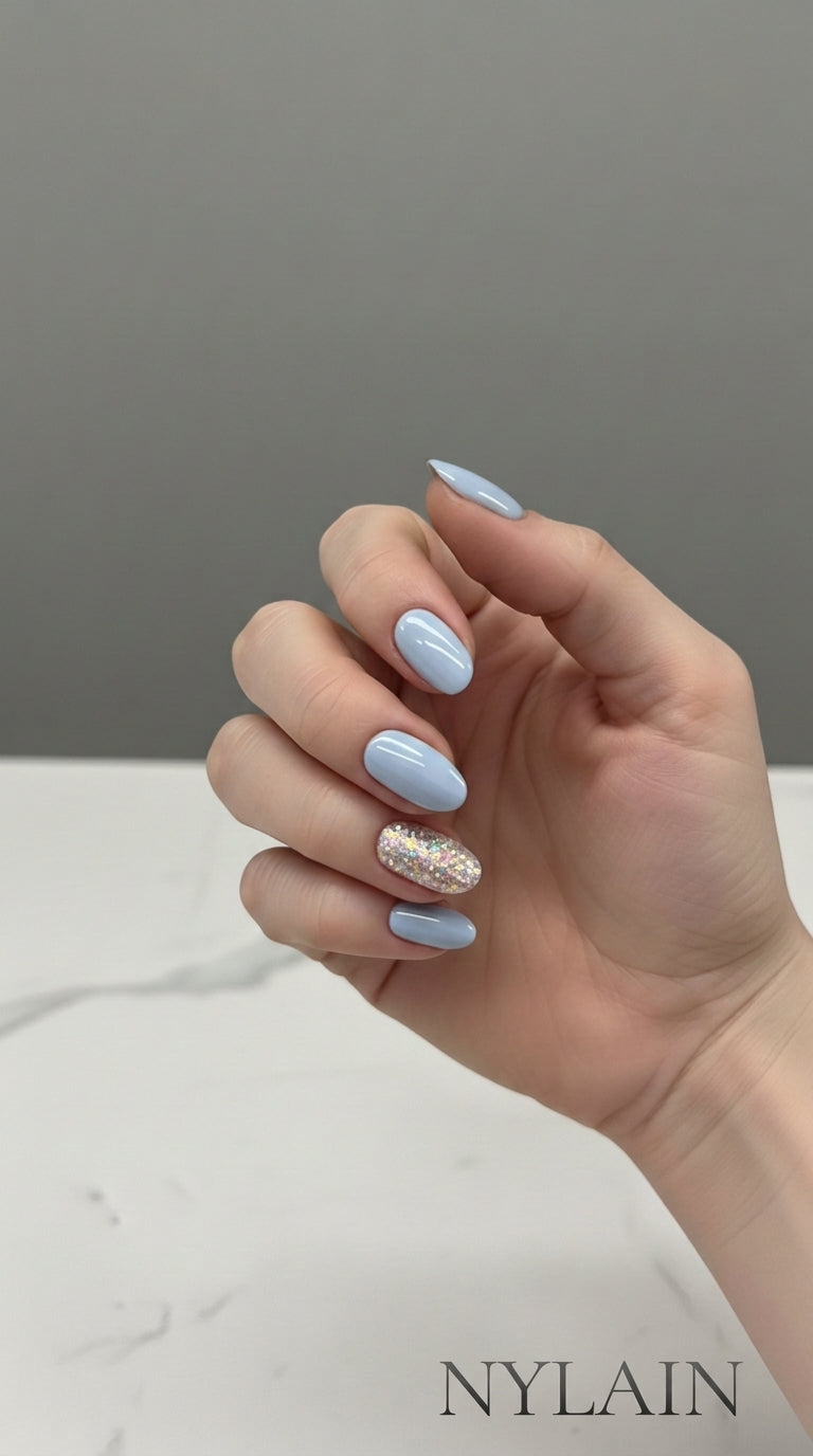 Hand with light blue nail and glitter wraps on a neutral background, featuring the brand NYLAIN.