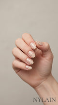 Hand with beige and silver polka dot nail wraps on a beige background, featuring the brand NYLAIN.