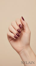 Hand with burgundy nail wraps on a beige background, featuring the Nylain brand.