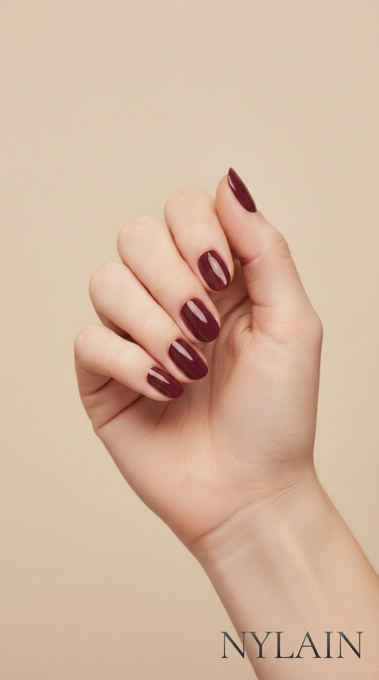 Hand with burgundy nail wraps on a beige background, featuring the Nylain brand.